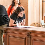 Nina Wadia studying the script, leaning on wooden plinth