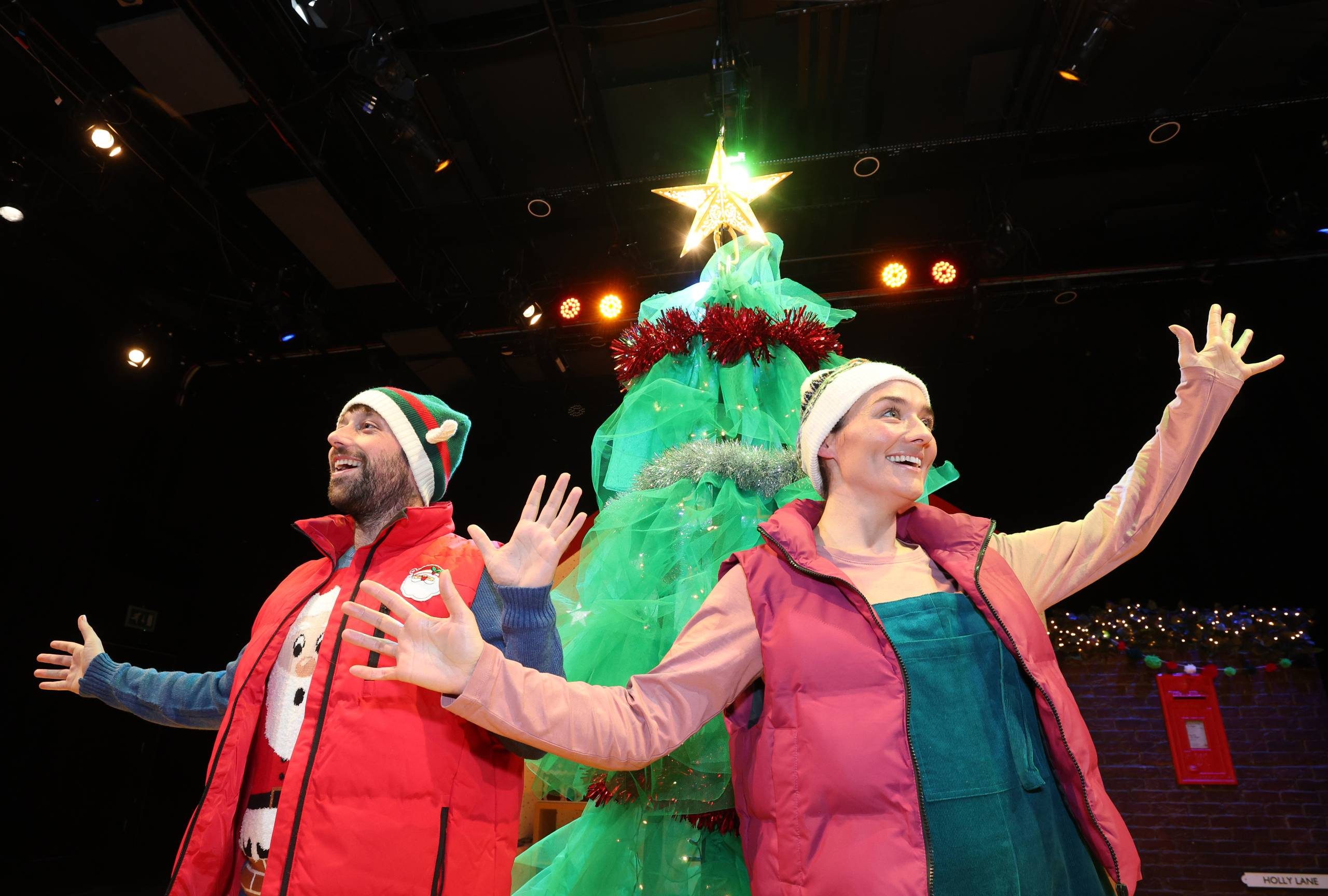 Male and female character stand in front of a tall Christmas tree with a glowing star on top