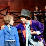 Young white male in a blue coat looking at another young white male wearing a black top hat and purple coat in a scene from our Summer Youth Project, Oliver!