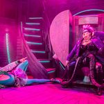 Triton (Thomas Lowe) lies on the floor, leotard dipping down to his waist where he wears a sparkly tutu, pointing at Ursula (Shawna Hamic) posing on a graffiti covered heart-shaped throne
