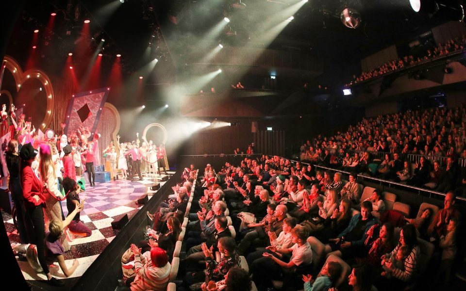 An image of MAST's studio one with a full audience. A colourful and bright performance of Alice in Wonderland is on stage.
