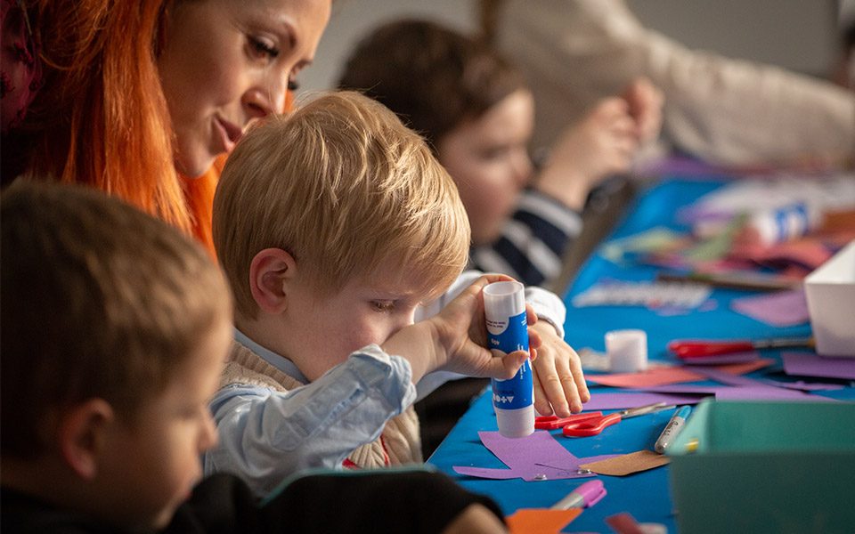 Young children sat at a table taking part in an arts and craft session at our Family Fun Day. The camera is focused on a young boy who is using a glue stick and some card.