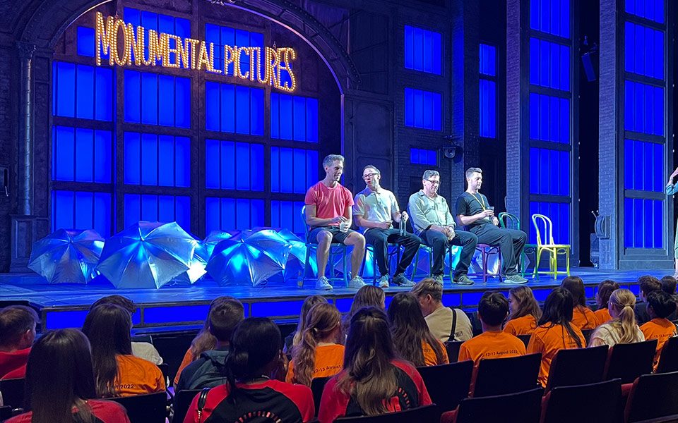 4 white men sat on stage taking questions from a diverse group of young children