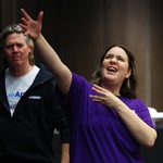 A woman in a purple t-shirt with her arm raised taking part in our 2022 Illuminate Drama Teachers Conference.