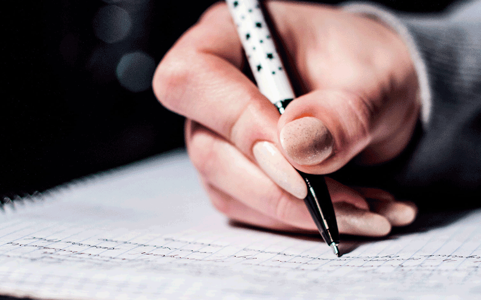 Close up shot of a hand holding a biro pen writing in a notebook.
