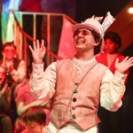 Young man with his arms raised perofrming on stage during our Christmas Youth Production of Alice, A Musical Adventure in Wonder;and