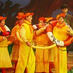 A group of young whte children in yellow and orange outfits looking bewildered on stage in a scene from our 2023 Summer Youth Project, Honk!