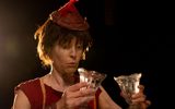 A female character hold two glasses and looks at them with intrigue.