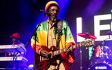 Bob Marley performer in green, yellow, red jacket and hat playing guitar