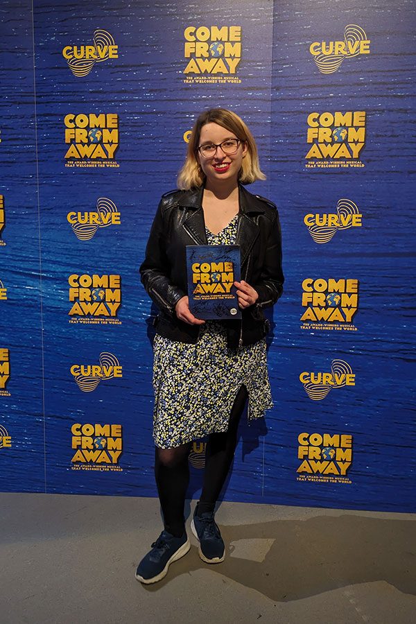 Lydia Greatrix stands in front of a Come From Away publicity board