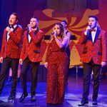 3 men and 1 woman in red glittery out fits sing together.