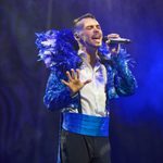 A passionate white male singer with blue glittery jacket with feather ruff and matching cummerbund.