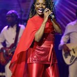Singing black woman in red trousers, top and cape.