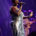Black short-haired woman in long sleeveless silver dress singing