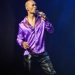 Black bald man in purple open-necked shirt singing