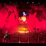 Real flames behind the singers and musicians on red lit stage, a guitar, bat and motorbike on the backdrop