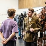 Chris Williams in military uniform, hat tucked under arm, talks earnestly to purple-shirted man, puppet horse behind him in the rehearsal studio