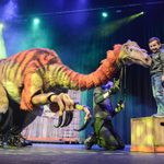 Boy on crate patting head of Segnosaurus puppet