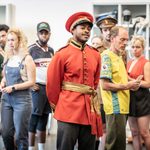 Daniel Rock in red military uniform, cast behind him in the rehearsal studio