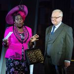 Oda Mae Brown (Jacqui Dubois) in bright pink jacket and large hat, watched on by Les Dennis in suit and tie.