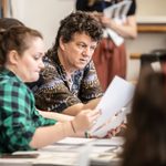 Tom Morris (Director) peering at notes held up by other creatives in rehearsal studio