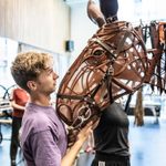 Tom Sturgess cradles life-sized head of brown puppet horse, looking up into his eyes.