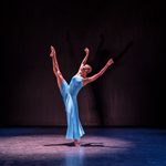 Black woman in long light blue dress with leg raised high in the air