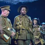 Sergeant Thunder (Gareth Radcliffe) stands next to a standing-to attention David Taylor (Ike Bennett) and ensemble in trench greens.