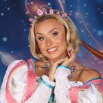 Princess Jill (Lauren Hampton) resting her face on her delicately clasped hands, smiling at the camera wearing pink jewelled tiara and pink and white dress