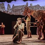 Albert Narracott (Tom Sturgess) kneels and blows into his hands as horse Joey (puppeteers Matthew Lawrence, Rafe Young, Felicity Donnelly) tilts his head towards him from behind