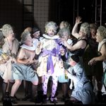 Marullo (Alastair Moore) in courtiers ruff and purple bow belt and tights, surrounded by cast in various states of dress