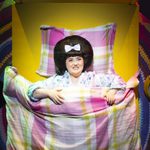 Tracy awake in pastel bed, large alarm clock at 7 o'clock next to her
