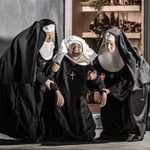 Two nuns support a third between them who is falling down laughing or crying