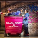 Neeta (Hiba Elchikhe) lies on top of pink industrial bin, holding hands with Ben (Dan Partridge) , the graffitied wall behind them reads you got no wall