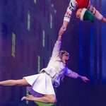 Woman in white dress and coat suspended in the air by man in Christmas jumper hanging above her.