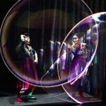 Two Asian women in long skirts and mismatched socks dance as projections of large bubbles hover before them