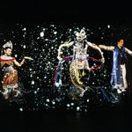 Projections on stage backdrop of three South Asian people in traditional dance dress and headdress, dancing
