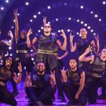 Diversity posing on purple lit stage, striking hand symbols