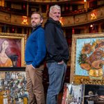 Peter Ash and man standing back to back in theatre surrounded by paintings