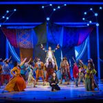 Joseph (Adam Filipe) in the technicolor coat, sitting on the shoulders on one of his brothers as the others and ensemble point up at him, the Narrator (Christina Bianco) kneels in front.