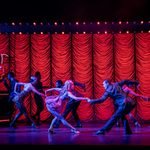 In a red washed bar, men and women dance, hands clasped as the bow low to each other