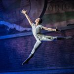 The Prince, in white with black boots, leaps outside brickwork and torn billboard