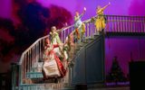 Four Regency women singing on a staircase with purple fog in the background, a Christmas tree under the stairs, and stockings hanging on the banister