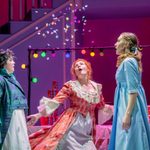 Three whit women, two in Regency dresses one in a frock coat with their hand in a pringles tube, look up at falling confetti, a table of snacks and multi-coloured lights behind them