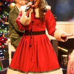 White woman in Santa dress singing into hand mic