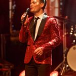 White man in sparkly red jacket singing into hand mic