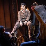 Calamity Jane (Carrie Hope Fletcher) laughs as she sits on top of a piano, a crowd looking up at her