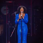 Whitney Houston in sparkly blue jumpsuit singing into standing mic