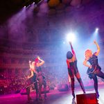 Rear view of four women in black corsets, tights and heeled boots, posing for theatre crowd