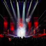 Audience pointing phones up at woman lit by spotlights, arm thrown up